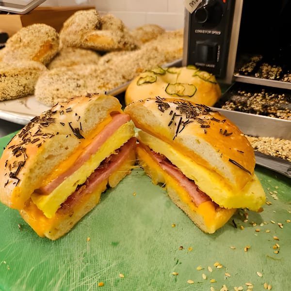 A sliced bagel sandwich with egg, cheese, and ham, with other bagels in the background.