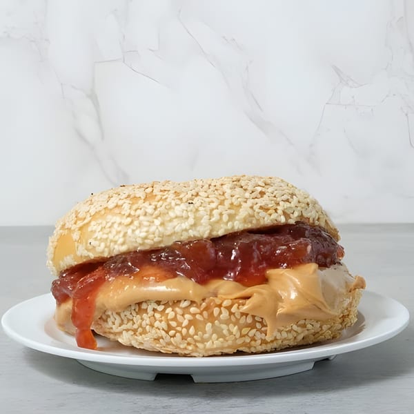 A sesame bagel with peanut butter and jelly on a white plate, against a marble background.