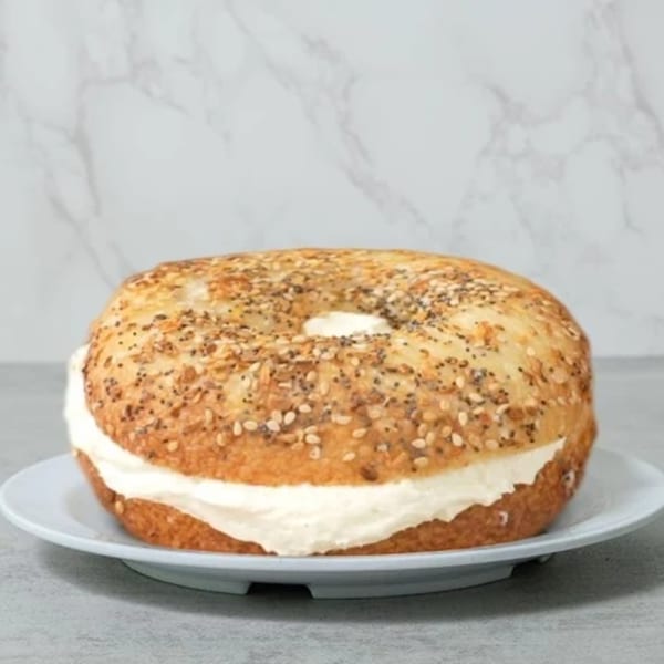 Everything bagel from Slice & Schmear, generously filled with cream cheese on a white plate.