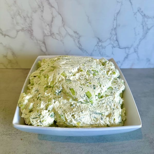 A large white rectangular dish filled with creamy cucumber dill cream cheese schmear.