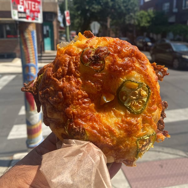 Hand holding a cheesy jalapeno bagel from Slice & Schmear on a sunny city street.